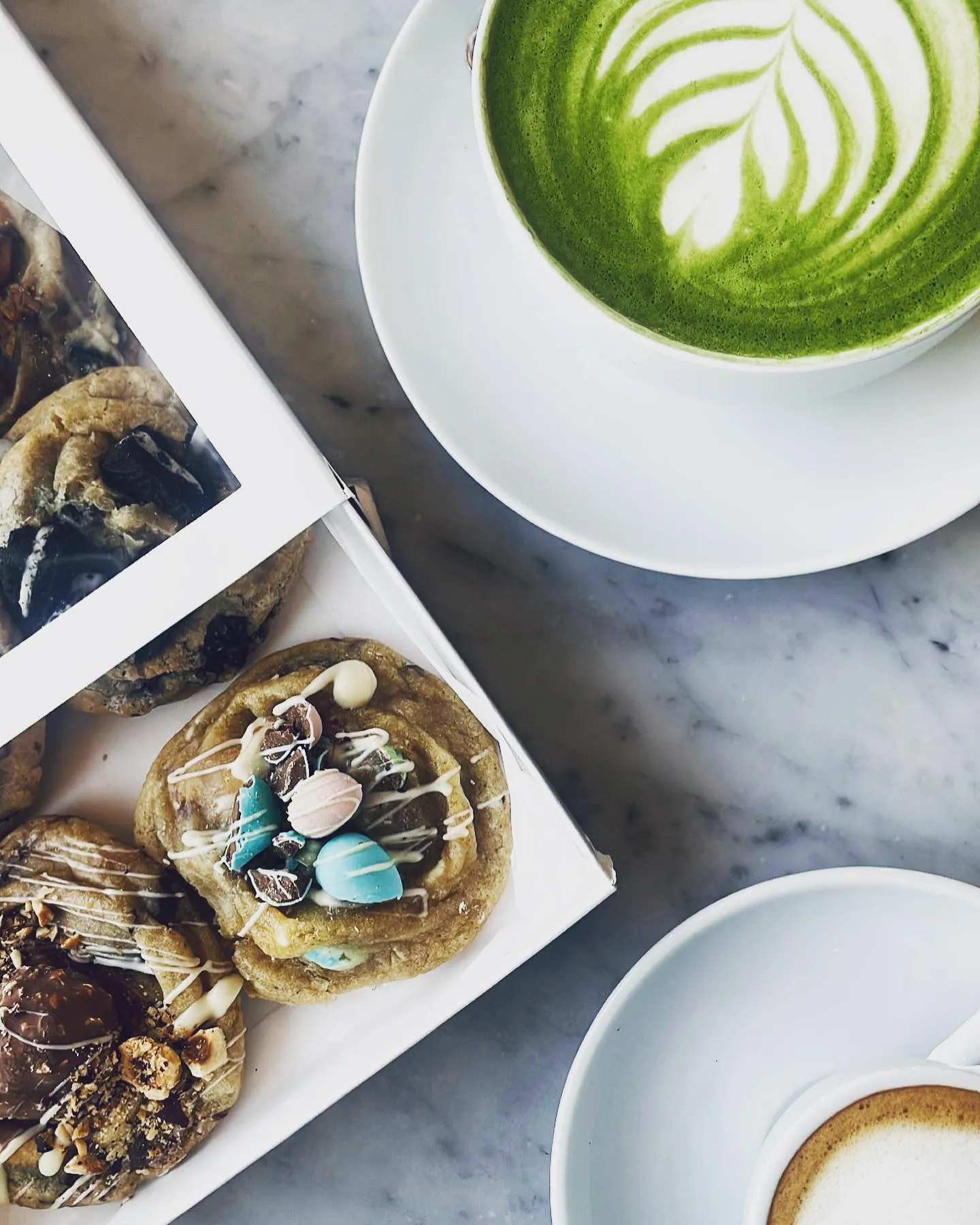 A box of Ro’s Dough cookies beside a matcha latte on a café table
